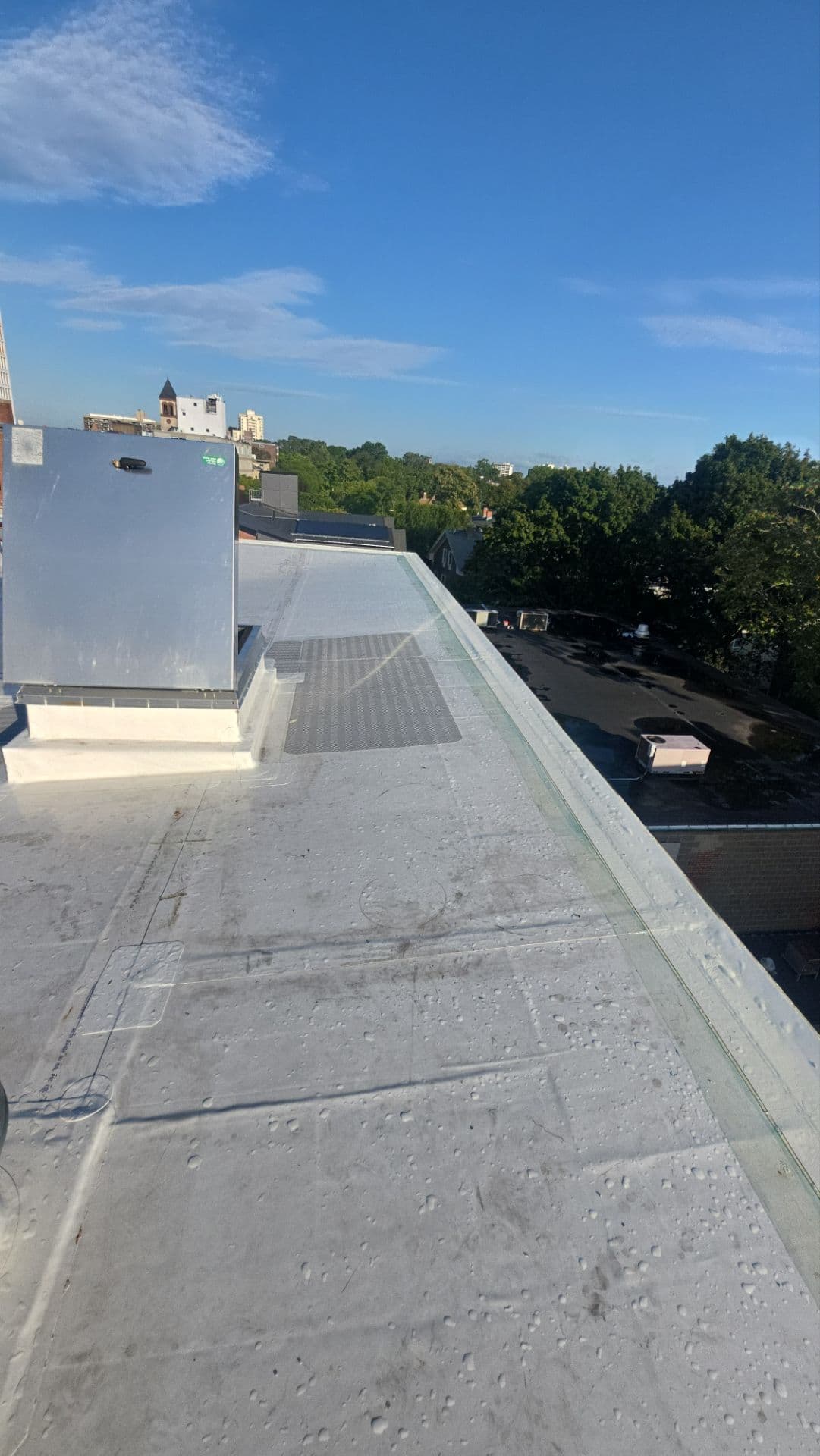 White membrane roof perimeter alongside rooftop equipment, curb flashing, and a gray walkway pad