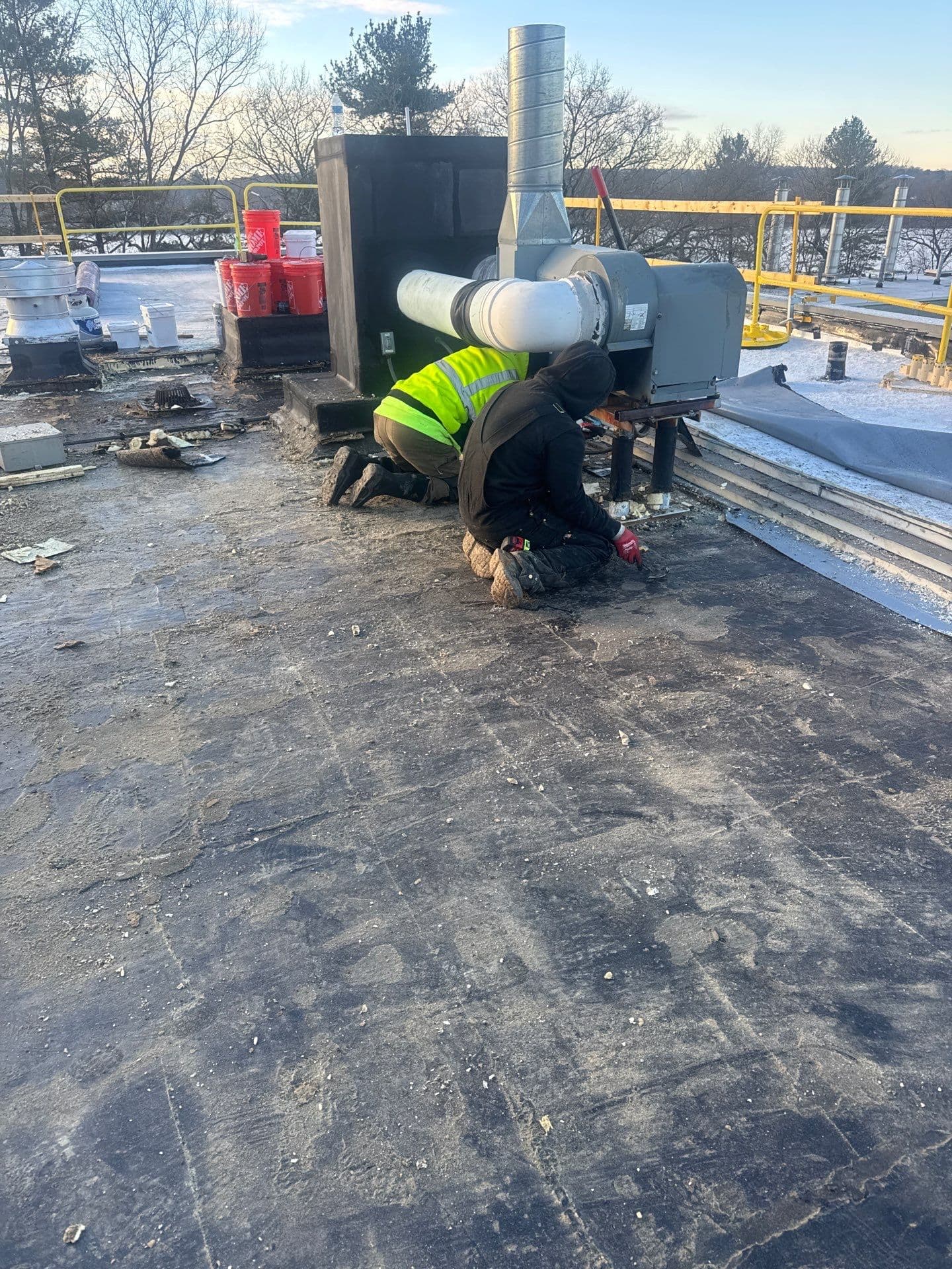 Roofers preparing the existing roof around a mechanical unit and its support legs at Natick Building 3