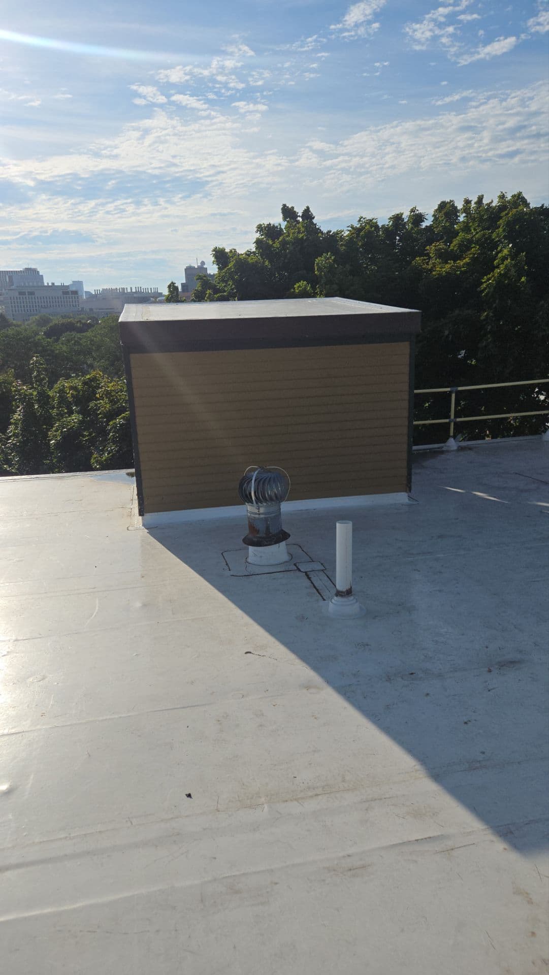 White membrane roof meeting a sided rooftop structure with a turbine vent and flashed pipe in front