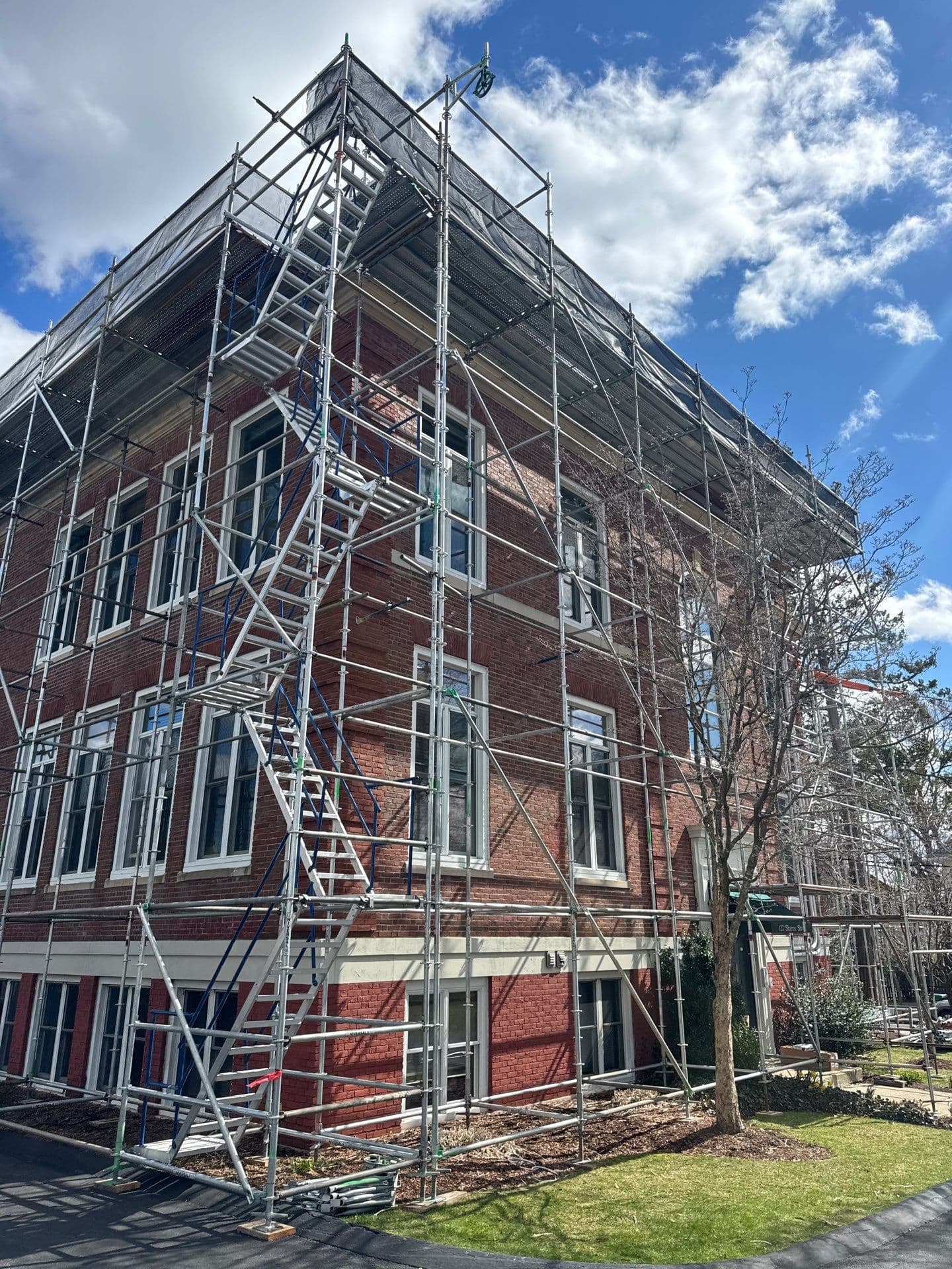 Wide corner view of the brick building surrounded by scaffold platforms, bracing, and stair access