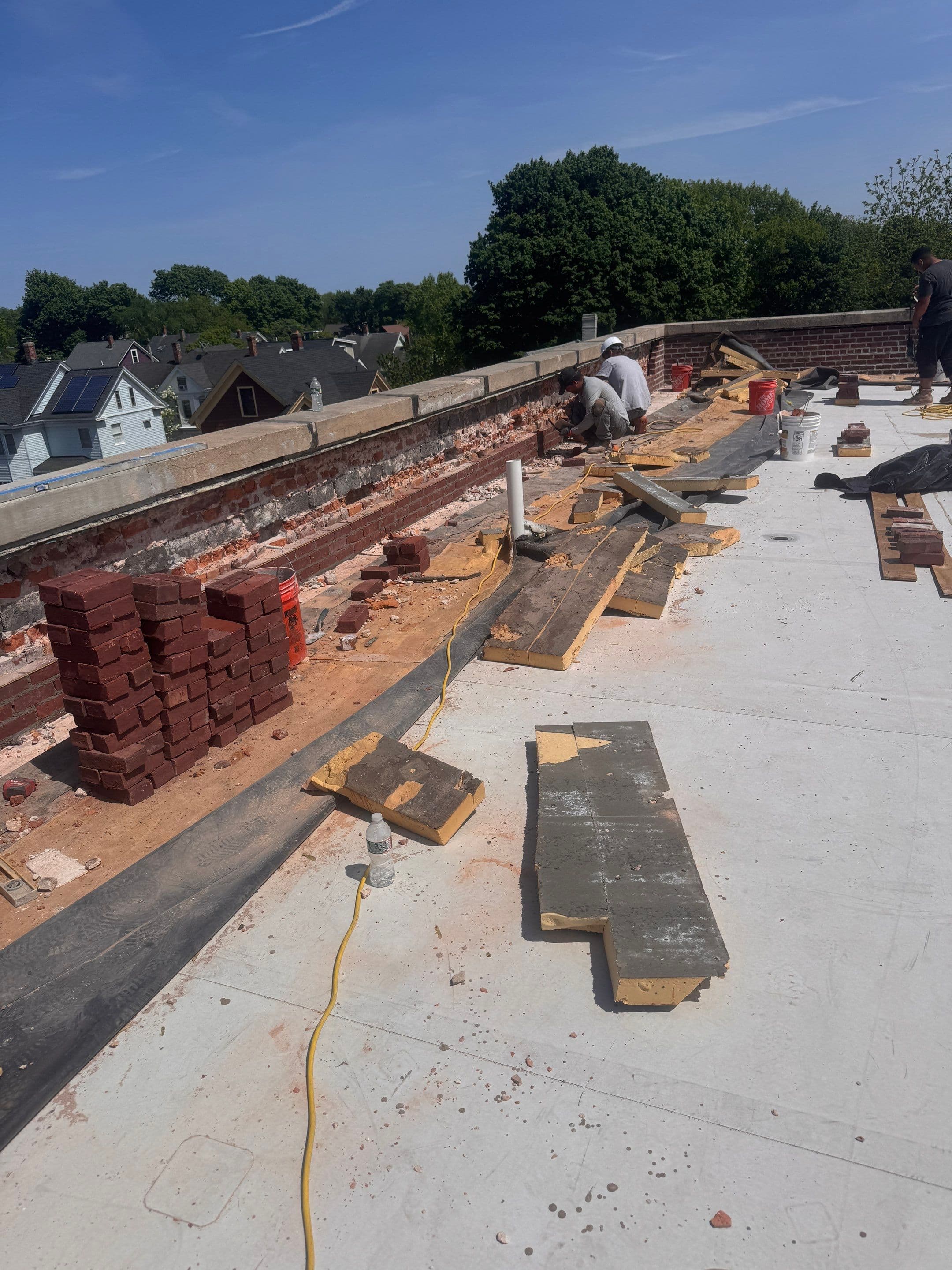 Workers rebuilding a brick parapet with bricks and masonry materials staged beside the work area