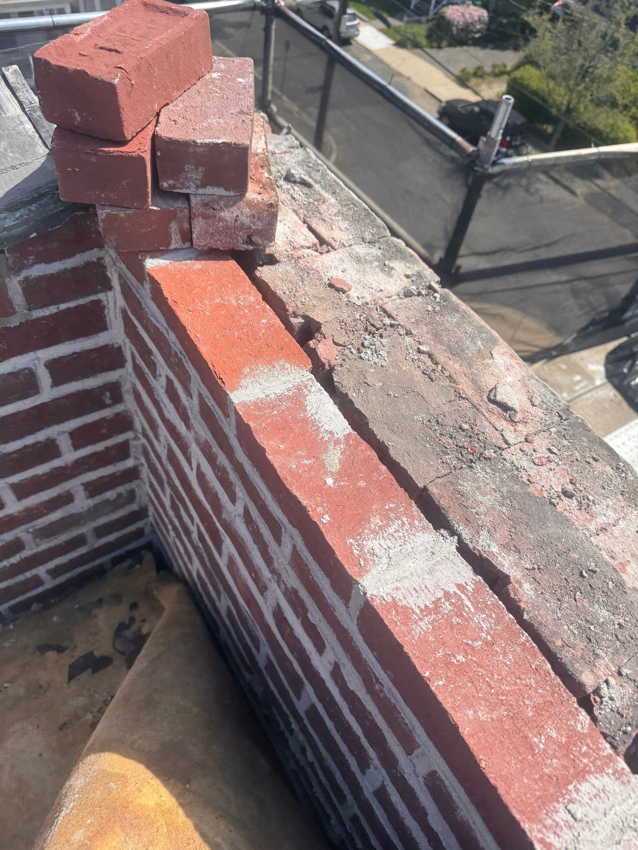 New brick courses and mortar joints at a parapet corner beside exposed existing masonry