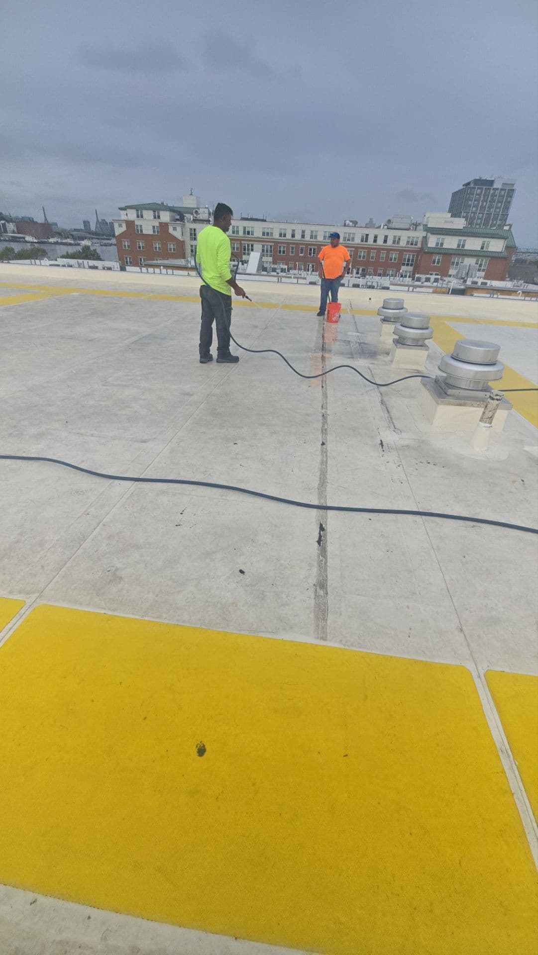 Workers washing a membrane roof beside equipment curbs and yellow walkway pads