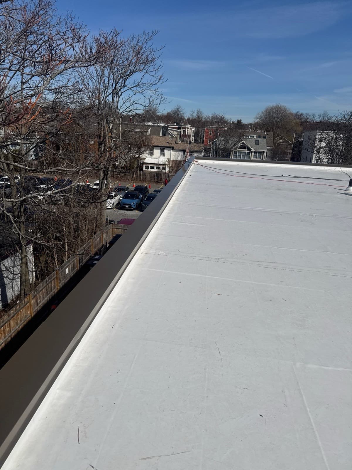 White roof membrane along the perimeter of a multifamily building with neighboring homes beyond